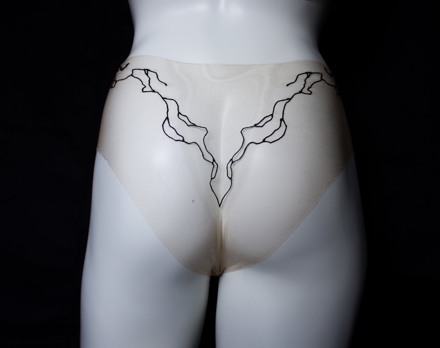 Mannequin wearing a beige garment with black abstract designs on a black background