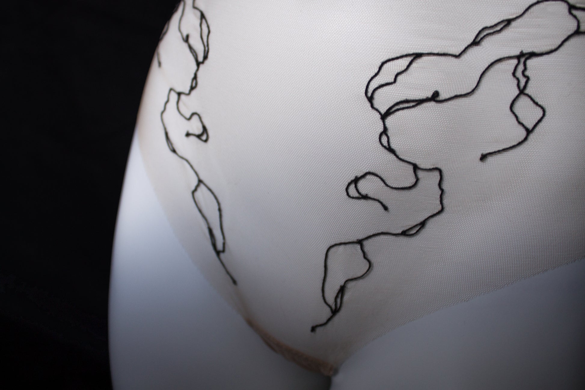 Close-up of a beige garment on a mannequin with a black line embroidery