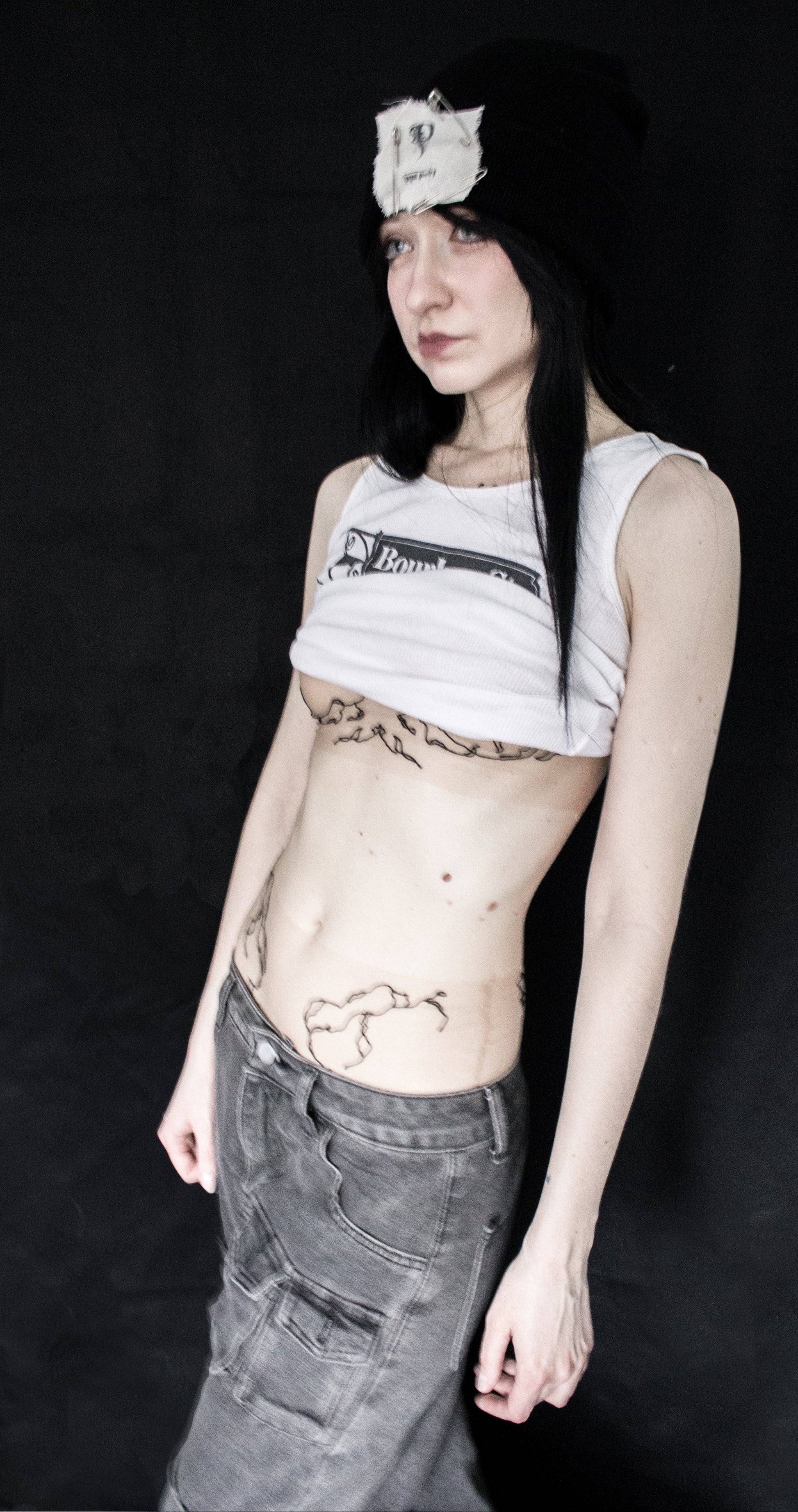 Person wearing a sleeveless top with a brand logo and dark pants against a black background